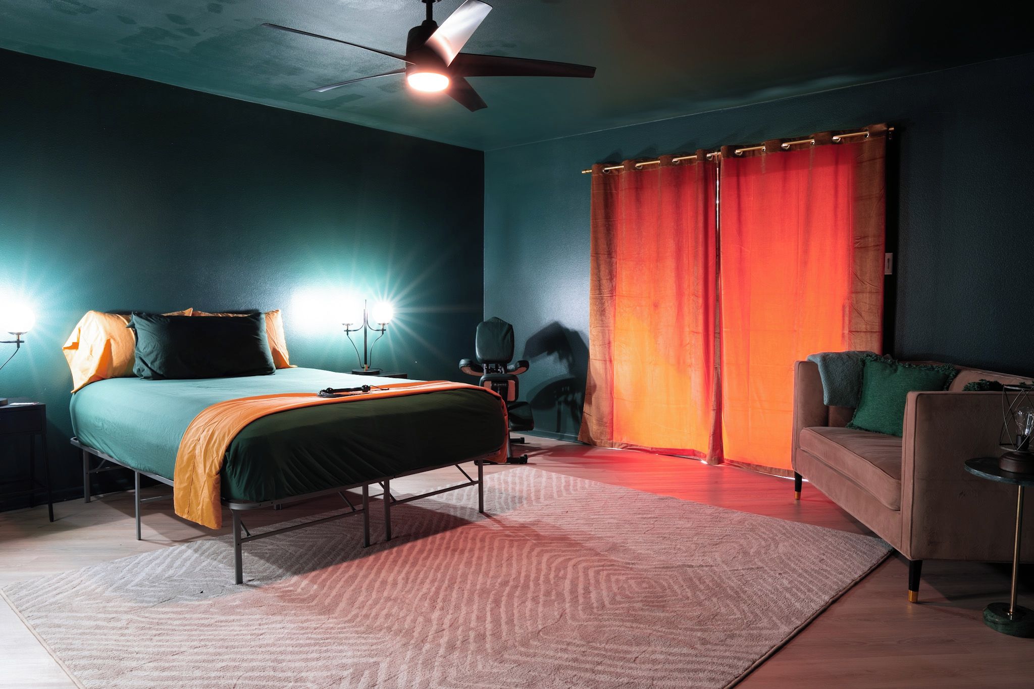 Een slaapkamer met een bed, bureau, stoel, bank, plafondventilator en een raam met gordijnen.