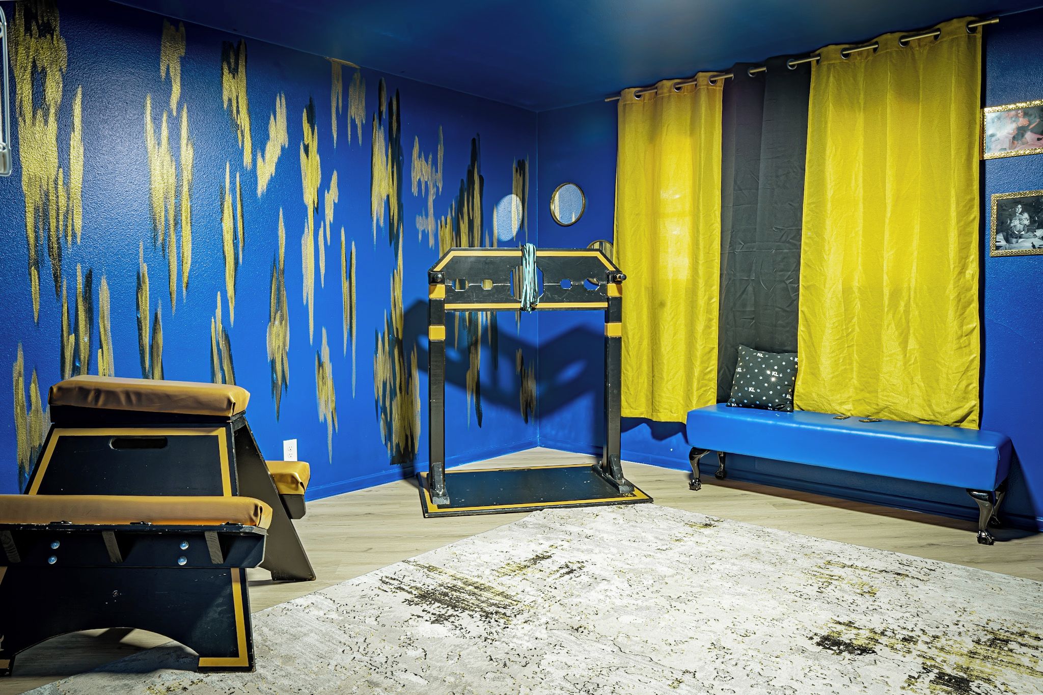 A room with a blue wall, a yellow curtain, a blue bench, and a black and yellow exercise equipment.