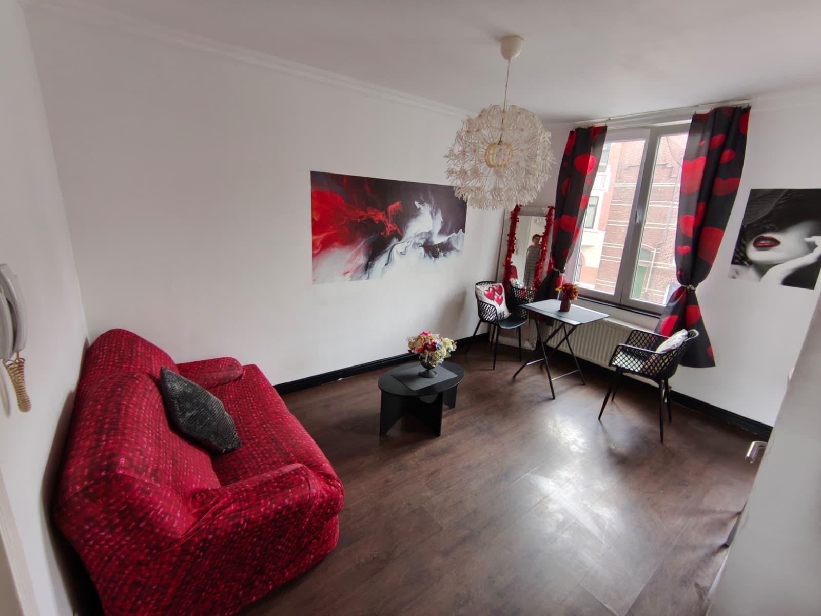 A modern living room with a red sofa, a dining table with chairs, and a large abstract painting on the wall.