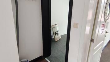 A hallway with a black-framed door leading to a room, a blue exercise machine, and a trash bin.