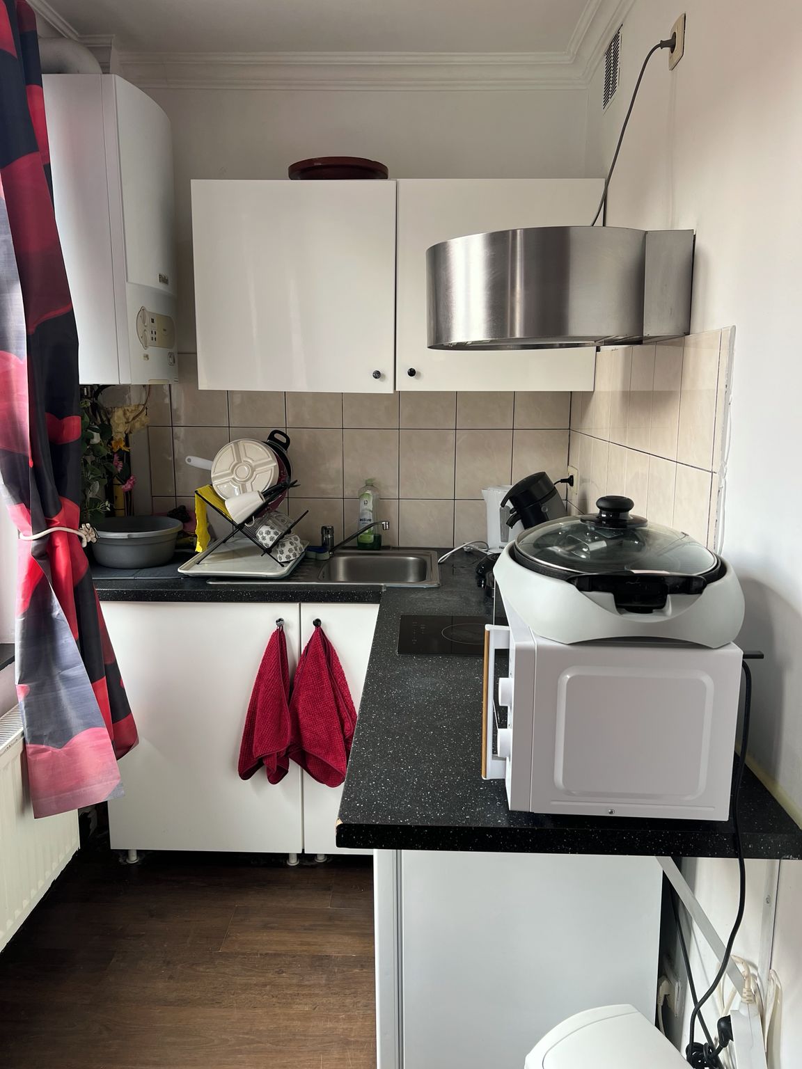 A kitchen with white cabinets, a stainless steel range hood, a black countertop, and a microwave.