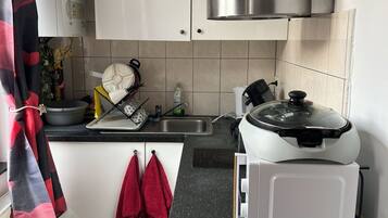 A kitchen with white cabinets, a stainless steel range hood, a black countertop, and a microwave.