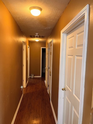A hallway with wooden flooring, white doors, and a ceiling light fixture.