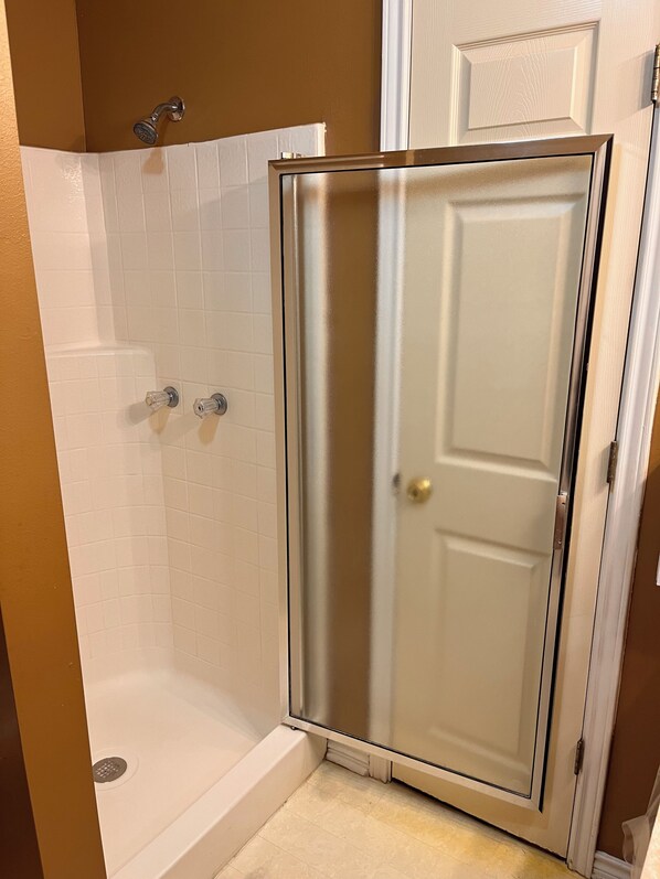 A bathroom with a glass-enclosed shower, white tiled walls, and a door with a brass handle.