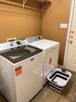Una lavadora y secadora Maytag de carga frontal en un cuarto de lavado con un cesto blanco.