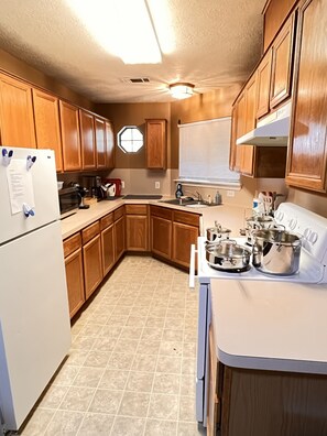 A kitchen with wooden cabinets, a white refrigerator, a stove, and a window with blinds.