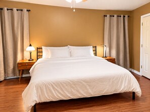 Un dormitorio con una cama, dos mesitas de noche, una lámpara y cortinas.