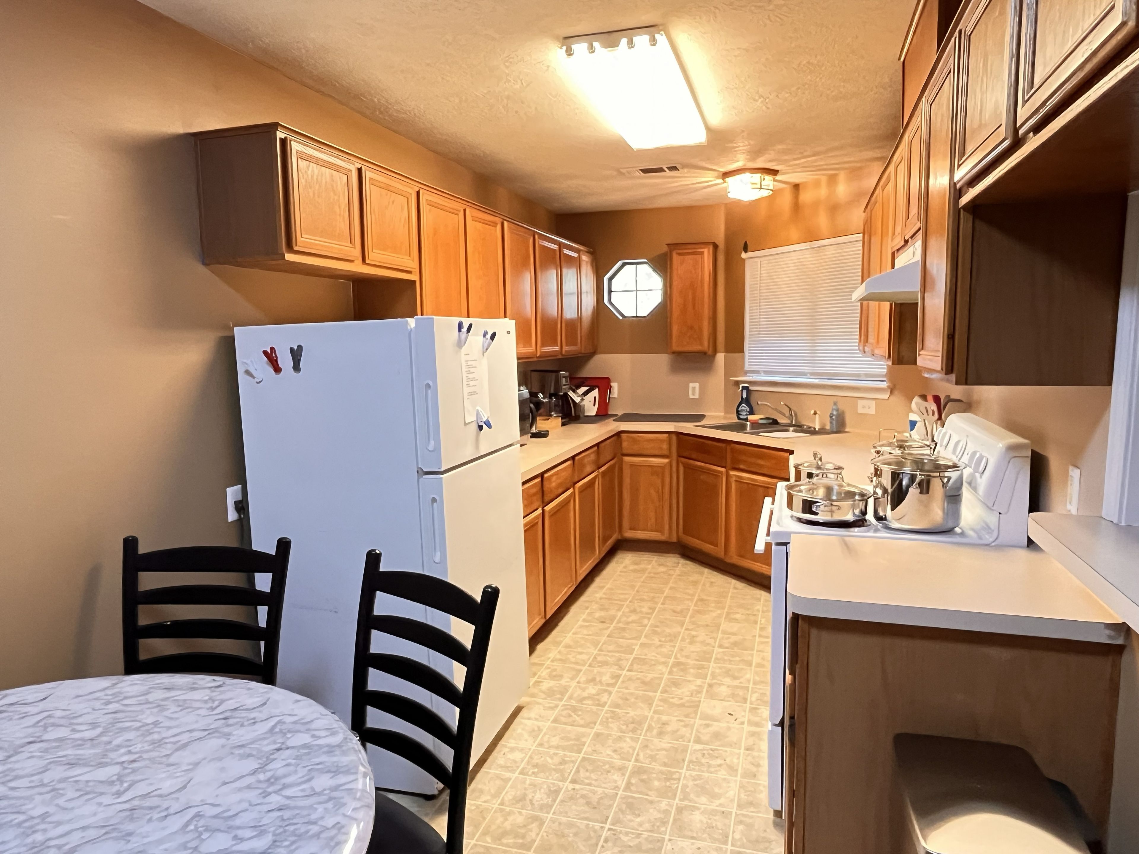 Une cuisine compacte avec des meubles en bois, un réfrigérateur blanc, un évier et un coin repas comprenant deux chaises et une table.