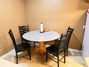 Una mesa redonda de comedor con cubierta de mármol, rodeada por cuatro sillas negras de patas de madera.