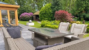 A patio area with wicker furniture, a glass-top table, and a gazebo. - Mereside House | Heated Indoor Pool, Hot Tub & Cinema (Allostock)