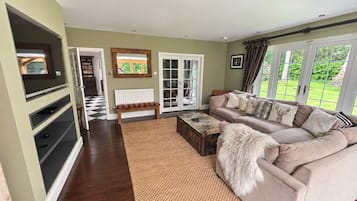 Ein Wohnzimmer mit einer Couch, einem Couchtisch, einem Fernseher und Blick ins Freie durch große Fenster.