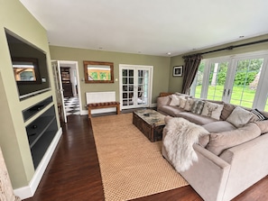 A living room with a sofa, a coffee table, a television, and a view of the outdoors through large windows.