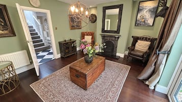 Un salon avec une cheminée, un lustre, une table basse en bois et un tapis à motifs.