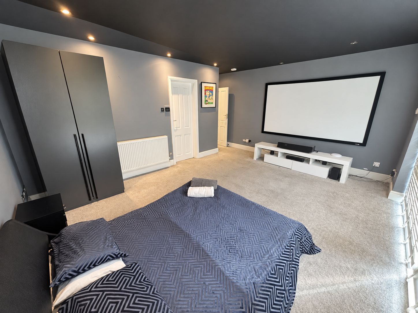 A bedroom with a bed, a TV, a white bench, and a door.