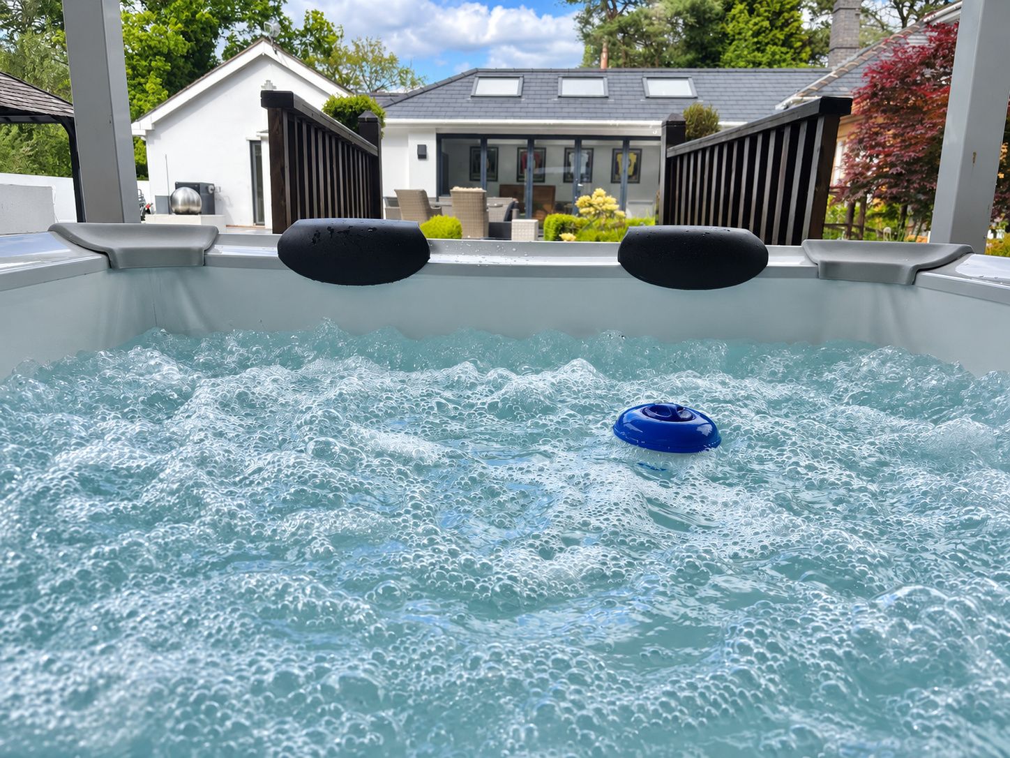 A hot tub with a blue float, surrounded by a white pool deck, with a house in the background.