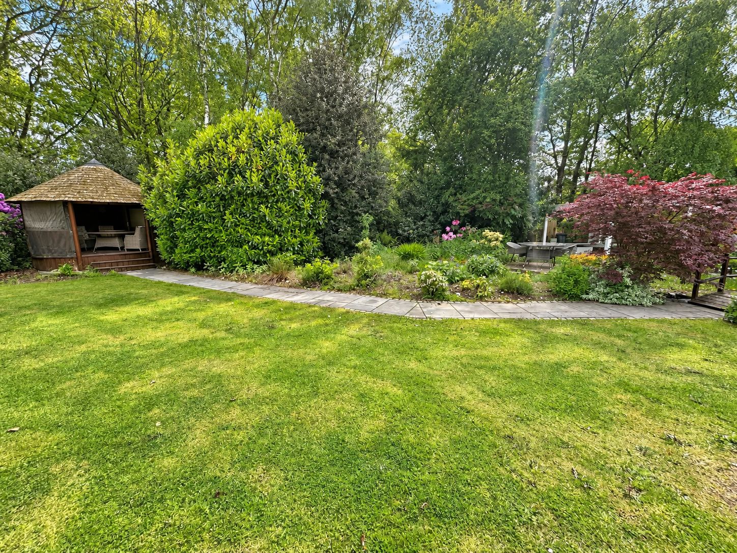 A well-maintained garden with a gazebo, various shrubs, and a lawn.