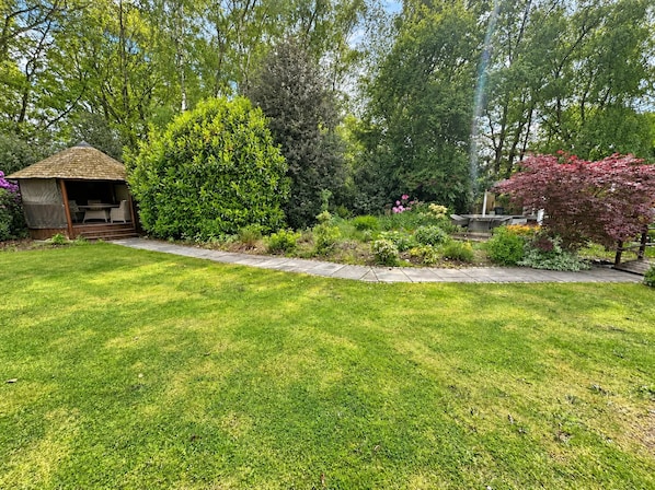 A well-maintained garden with a gazebo, various shrubs, and a lawn.