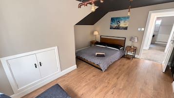 A bedroom with a sloped ceiling, a bed with a patterned bedspread, a bedside table with a lamp, and a wall-mounted picture.