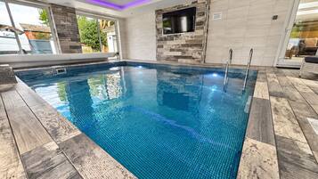 A swimming pool with a tiled edge, a built-in TV, and a wooden deck surrounding it.