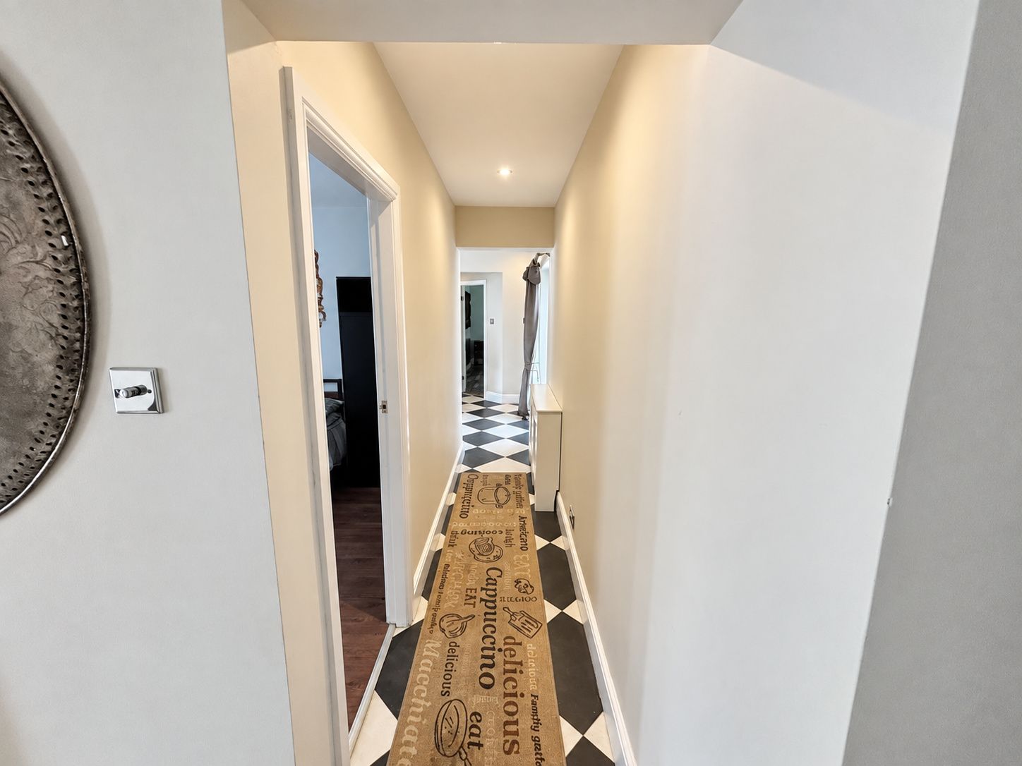 Ein Flur mit einem Schachbrettmuster auf dem Boden, einer Tür zu einem Schlafzimmer und einer Wandleuchte.