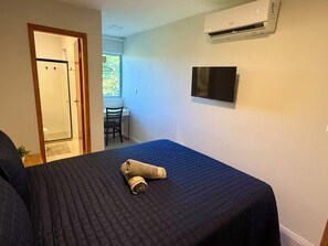 A hotel room with a bed, a TV mounted on the wall, and a window with a view of greenery. - 2-bedroom village house in Imbassai Beach, Bahia, 5 minutes from the beach, close to the sea! (Mata de São João)
