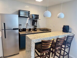 A modern kitchen with a built-in refrigerator, microwave, coffee maker, and gas stove. There are bar stools and pendant lights. - 2-bedroom village house in Imbassai Beach, Bahia, 5 minutes from the beach, close to the sea! (Mata de São João)