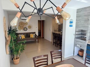 Ein modernes Wohnzimmer mit einer Couch, einem Esstisch, Stühlen und einer Deckenleuchte.