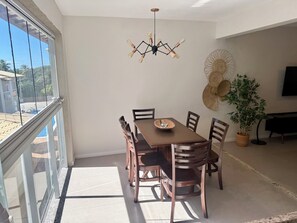 A dining area with a table and chairs, a ceiling light fixture, a wall-mounted fan, and a potted plant. - 2-bedroom village house in Imbassai Beach, Bahia, 5 minutes from the beach, close to the sea! (Mata de São João)