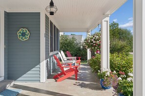 Eine Veranda mit überdachter Sitzgelegenheit, eine Tür mit Hausnummer und ein Garten mit Blumen.