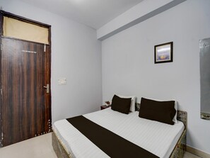 A room with a bed, a wooden door, a wall-mounted picture, and a small table with a plant.