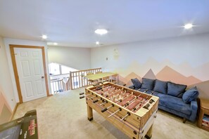 A room with a foosball table, a blue sofa, and a staircase leading to an upper level. - Lakefront Retreat, relaxation with A/C, Game Room, boating, epic yard & views (Pocono Summit)