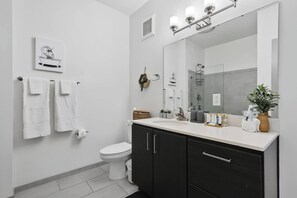Une salle de bain moderne avec un lavabo blanc, des meubles sombres, un grand miroir et des toilettes.