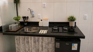 Una cocina con un lavamanos de acero inoxidable, una estufa a gas, un cubo de basura y una planta en maceta.