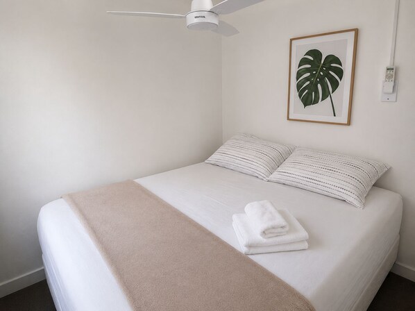 A neatly made bed with a white comforter and two pillows, a beige throw blanket, and a folded white towel on the bed.