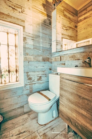 A bathroom with a rustic wooden wall, a white toilet, and a wooden vanity. - Patina | Local Charm By The Sea | La Cala Beach (Las Lagunas de Mijas)