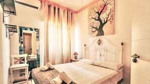 Ein Schlafzimmer mit einem Bett, einem Nachttisch, einem Sessel, einem Gemälde und einem Fenster mit Vorhängen.