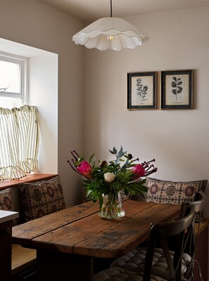 A dining area with a wooden table, a vase with flowers, and a hanging light fixture. - Charming Two Bedroom Cottage in Malmesbury (Malmesbury)