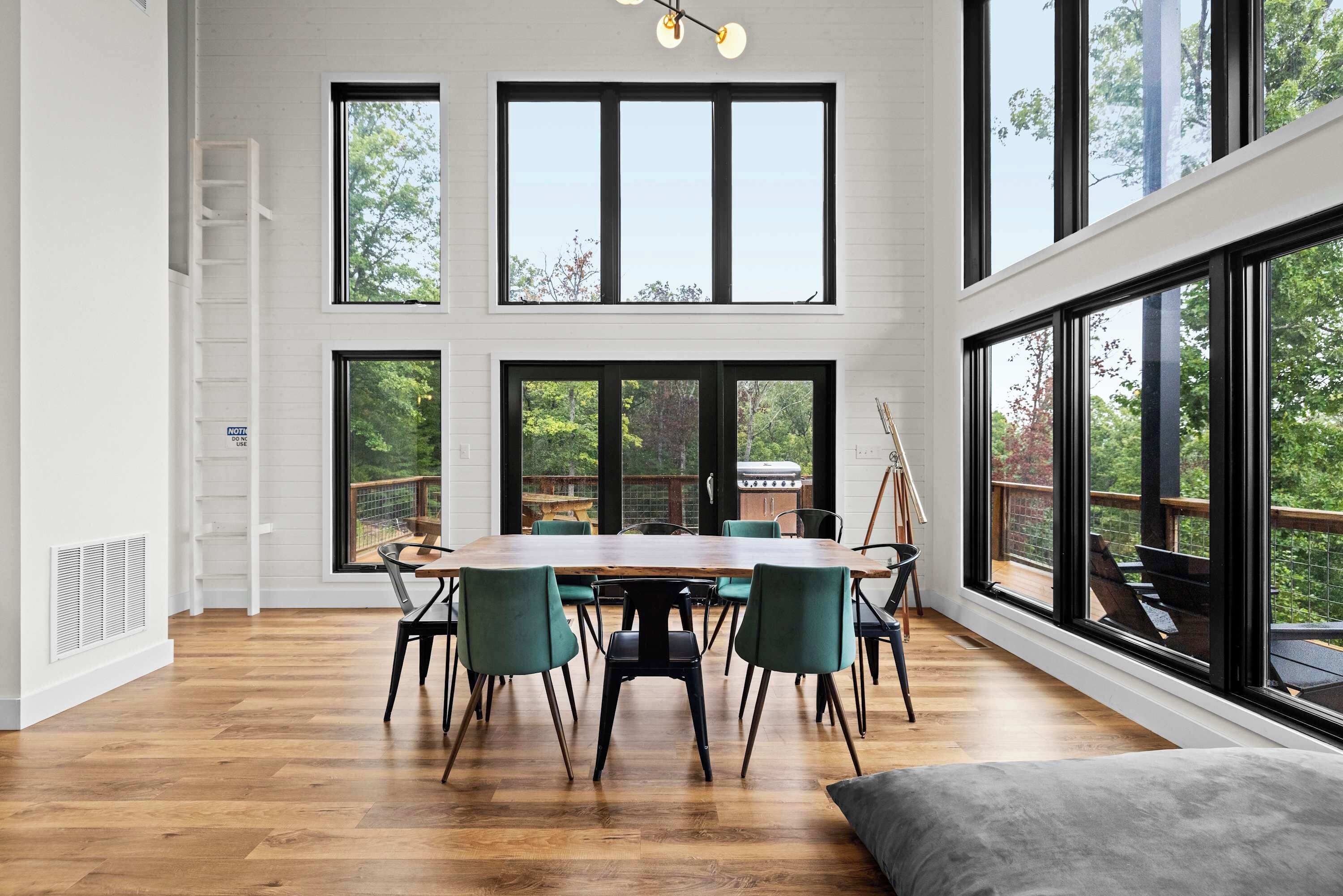 A dining area with a wooden table and chairs, large windows, and a view of the outdoors.