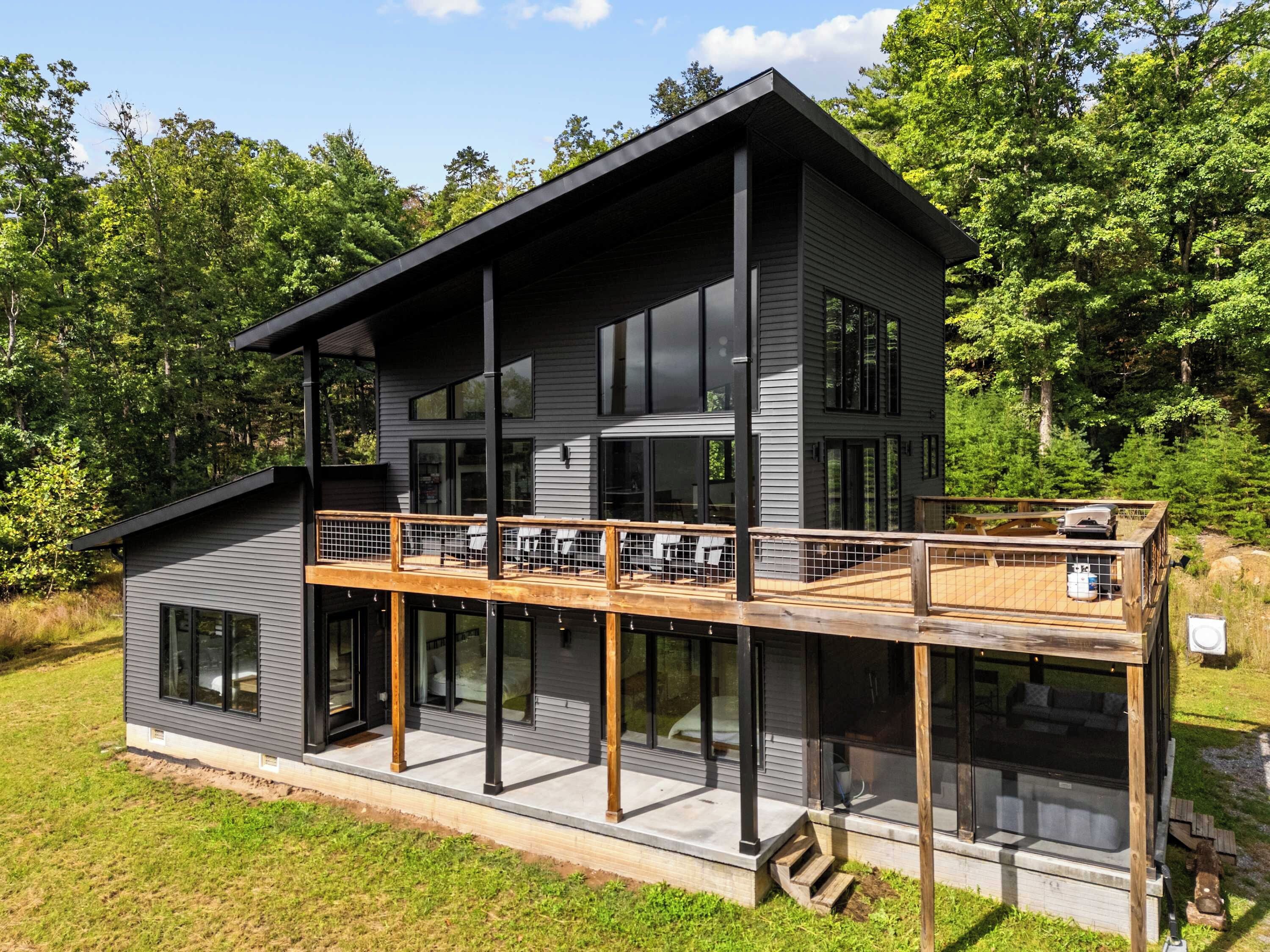 A modern two-story house with a balcony, large windows, and a deck.