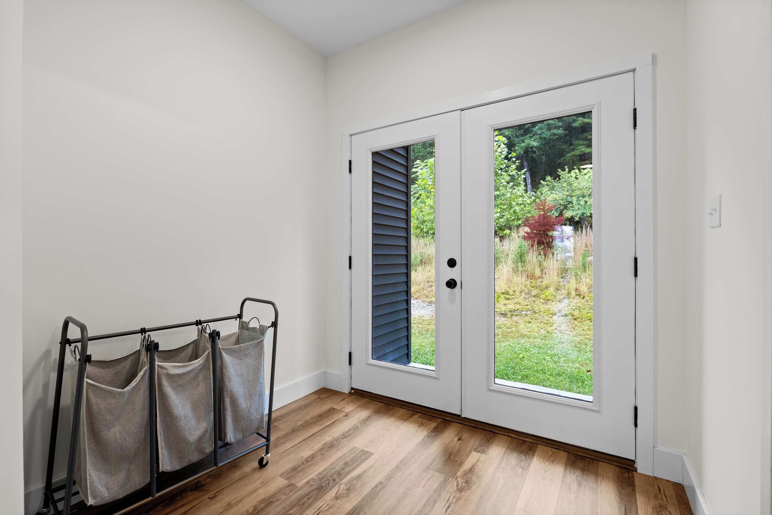 A room with a wooden floor, a white door with a window, and a metal cart with bags.