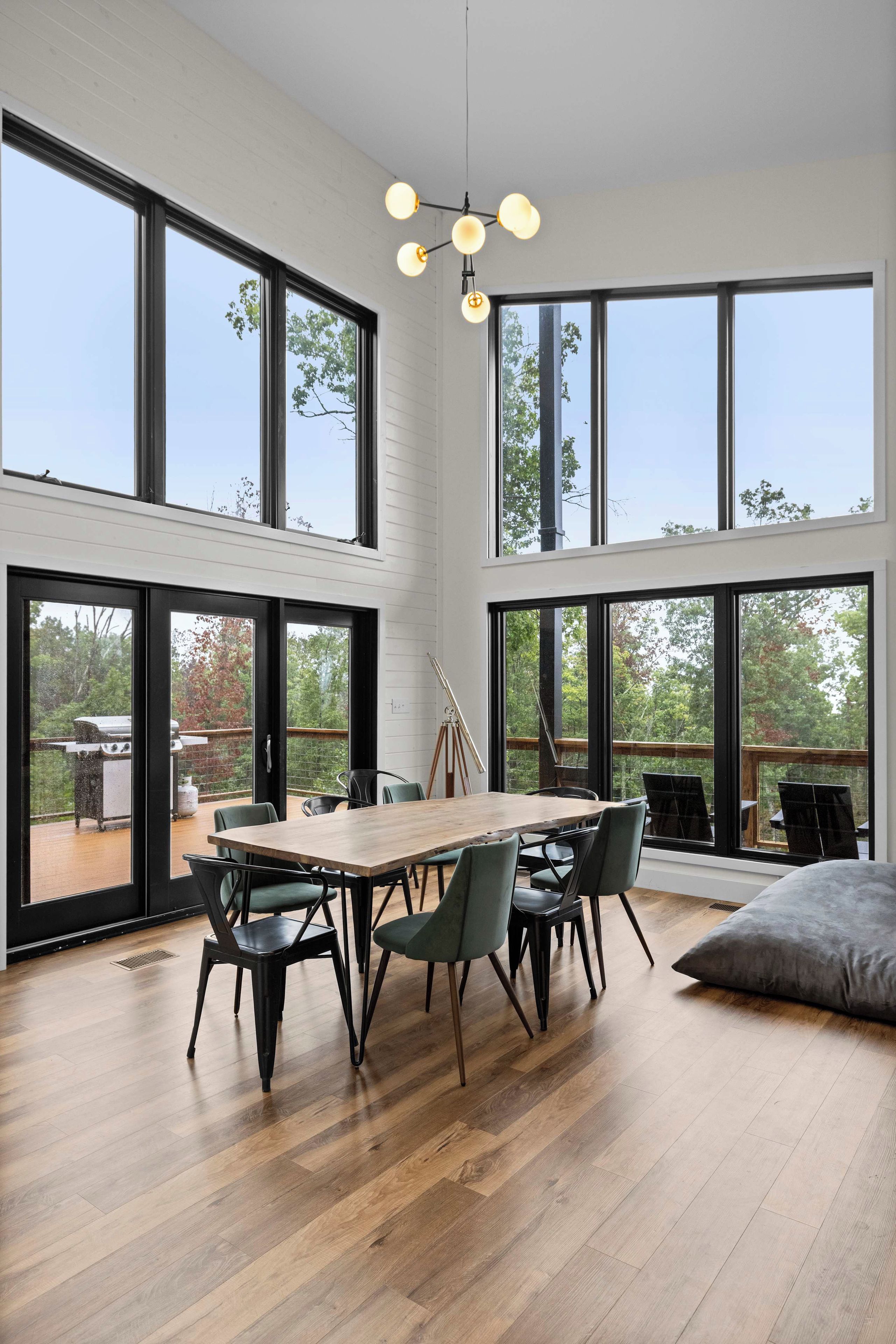 Een ruime kamer met een grote eettafel, meerdere stoelen en uitzicht op het landschap door grote ramen.