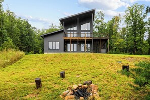 A modern two-story house with a large deck and a fire pit in the front yard.