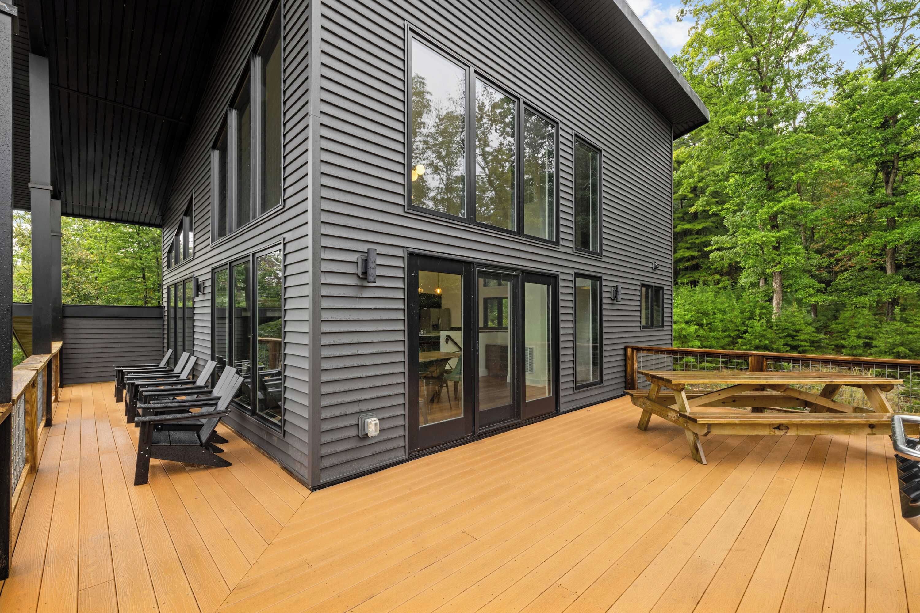 A modern two-story house with a deck, large windows, and a view of a forest.