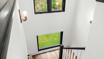 A modern staircase with a wooden handrail and a view of a green outdoor area through large windows.