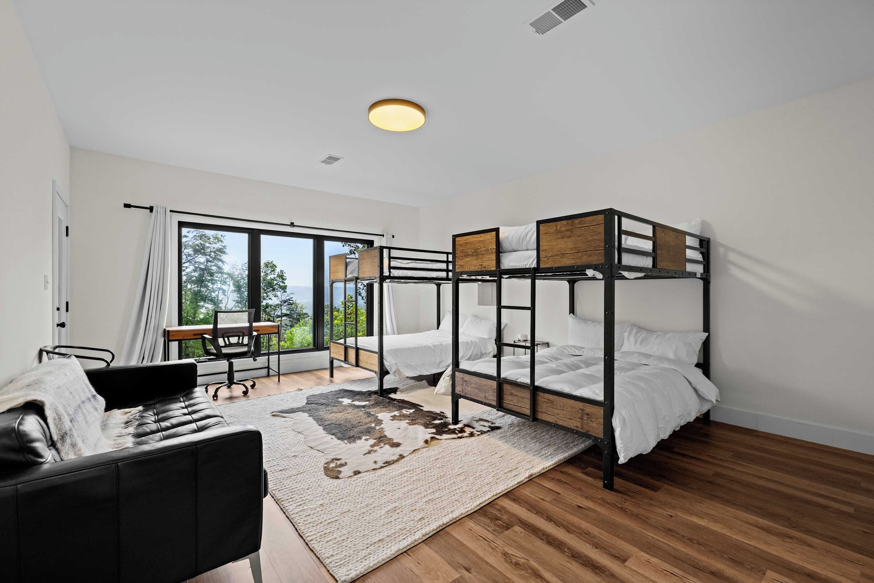 A modern bedroom with bunk beds, a desk, and a view of greenery outside.