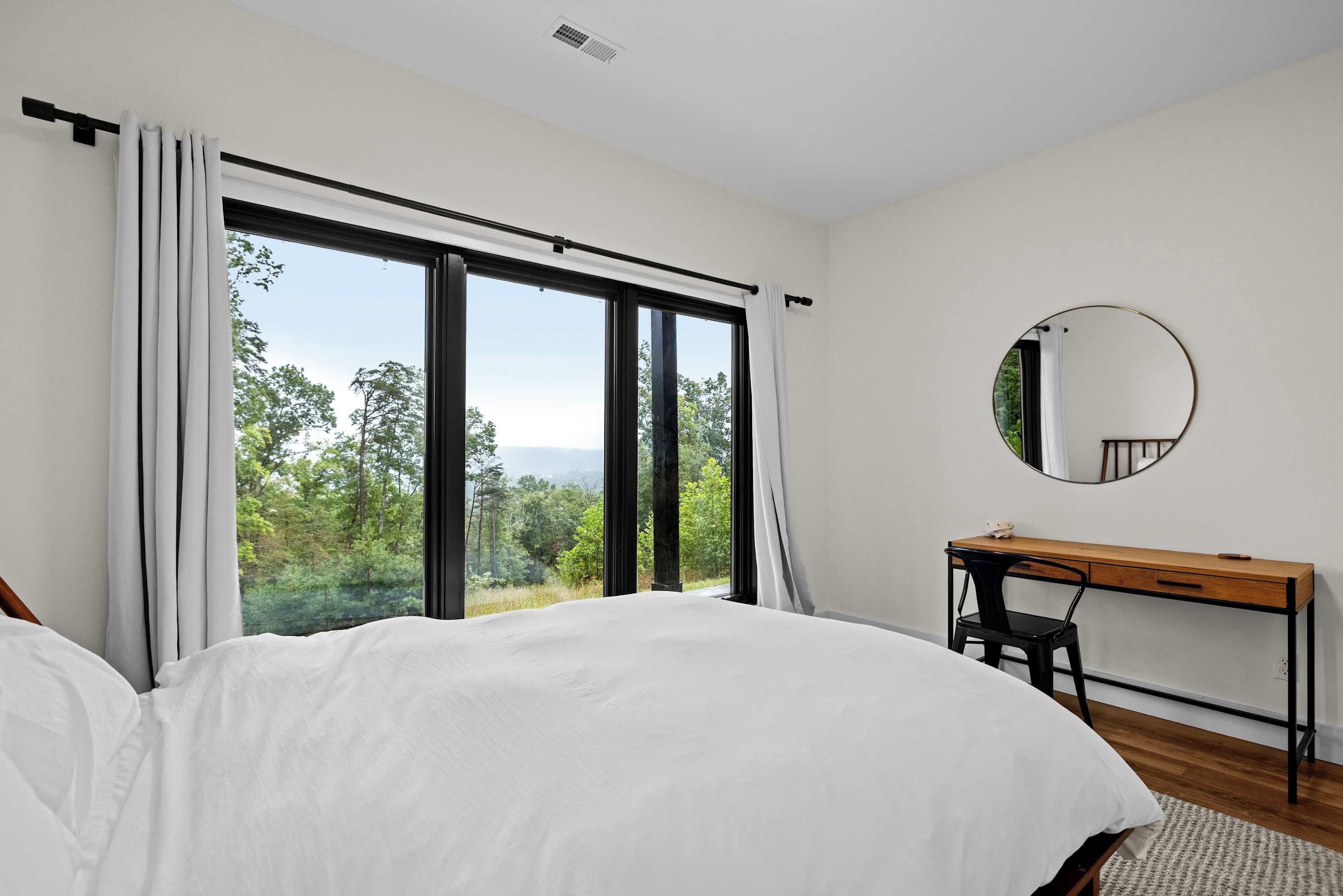 A bedroom with a large window, a bed, a desk, and a chair.