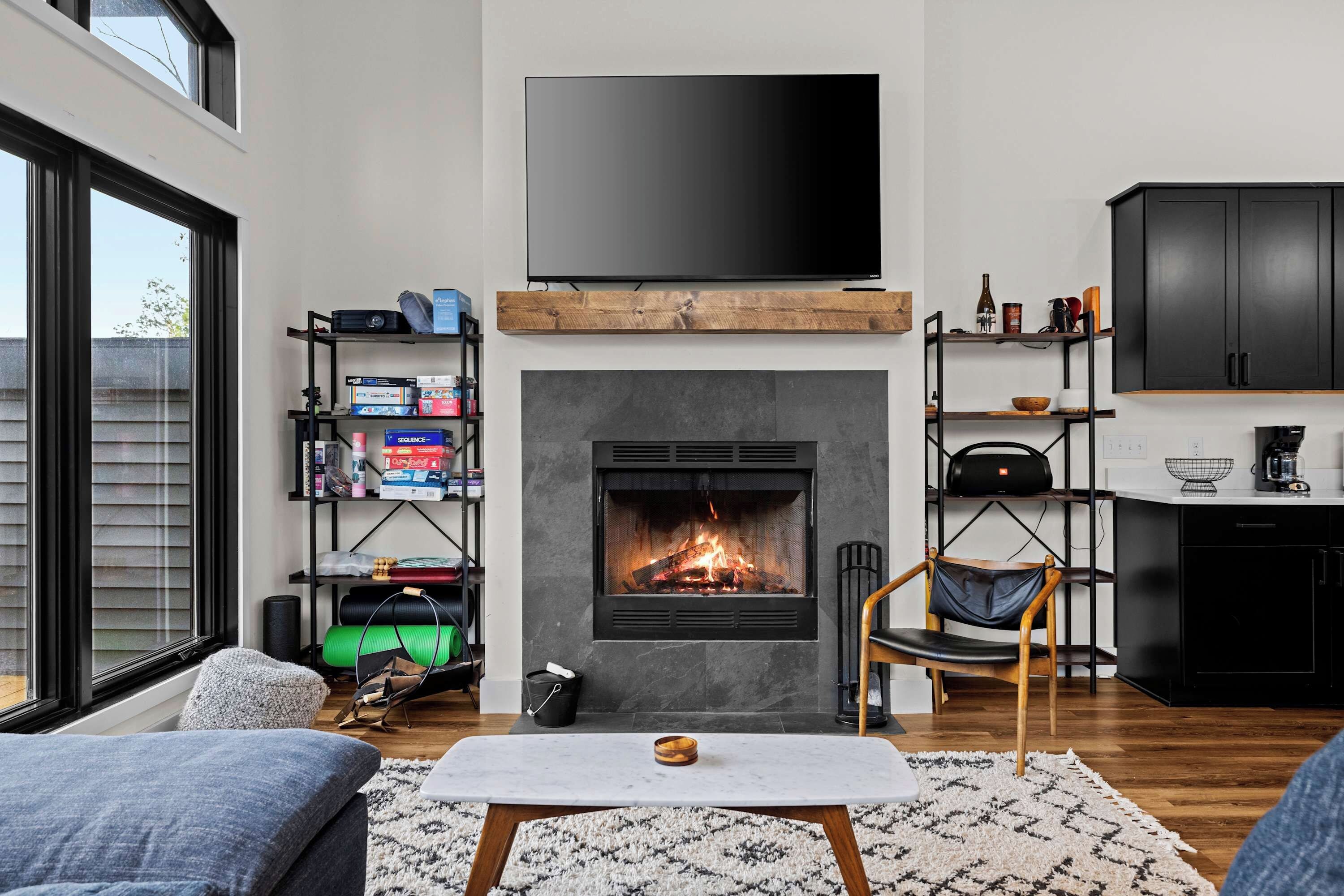 Uma sala de estar moderna com lareira, uma TV de tela plana acima dela e uma estante cheia de diversos objetos.
