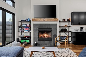 A modern living room with a fireplace, a flat-screen TV mounted above it, and a bookshelf filled with various items.
