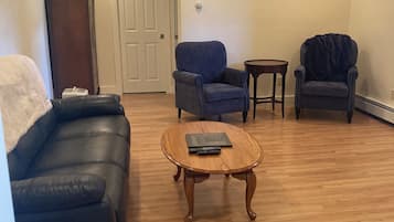 Ein Wohnzimmer mit einem schwarzen Ledersofa, zwei Sesseln, einem Holztisch und einem kleinen runden Tisch.