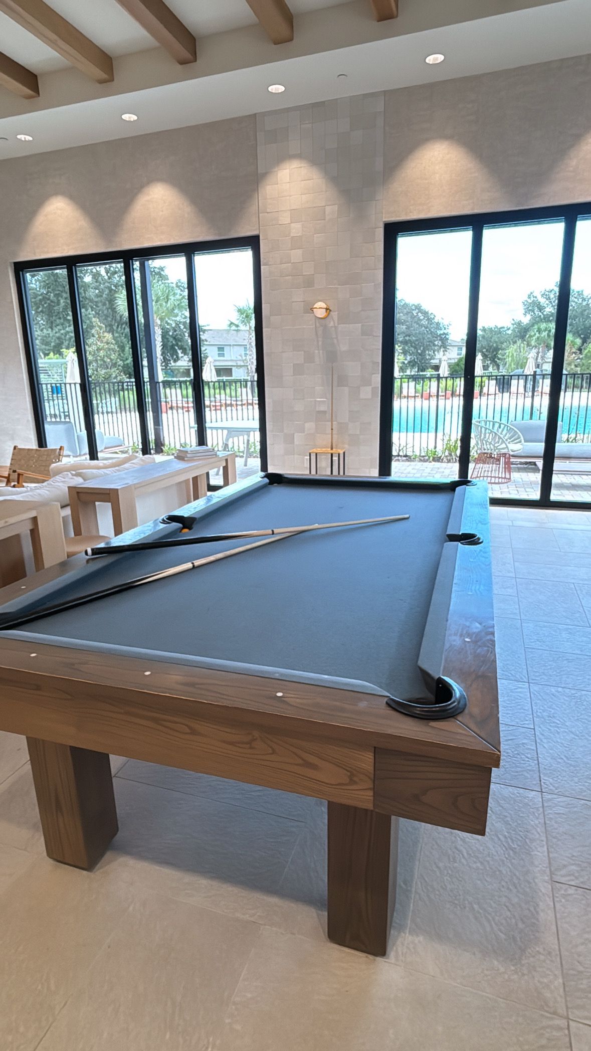 A pool table in a room with large windows, a bench, and a view of a pool outside.